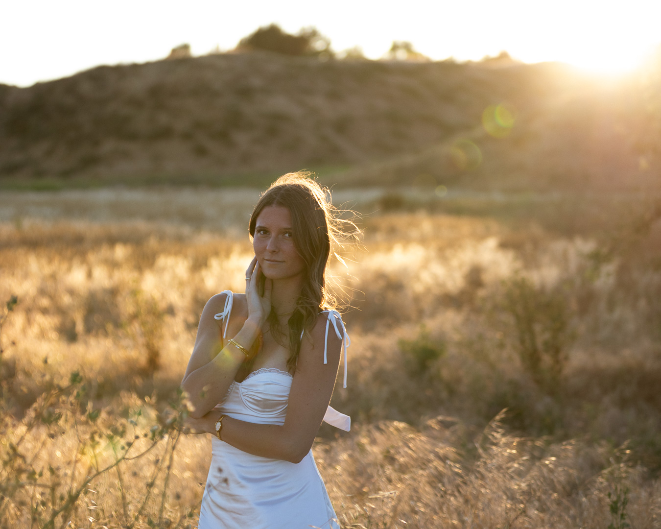 Woman in a white dress in a sunlit golden field with hills behind her